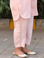 Person wearing light pink pants and white shoes on a sidewalk.