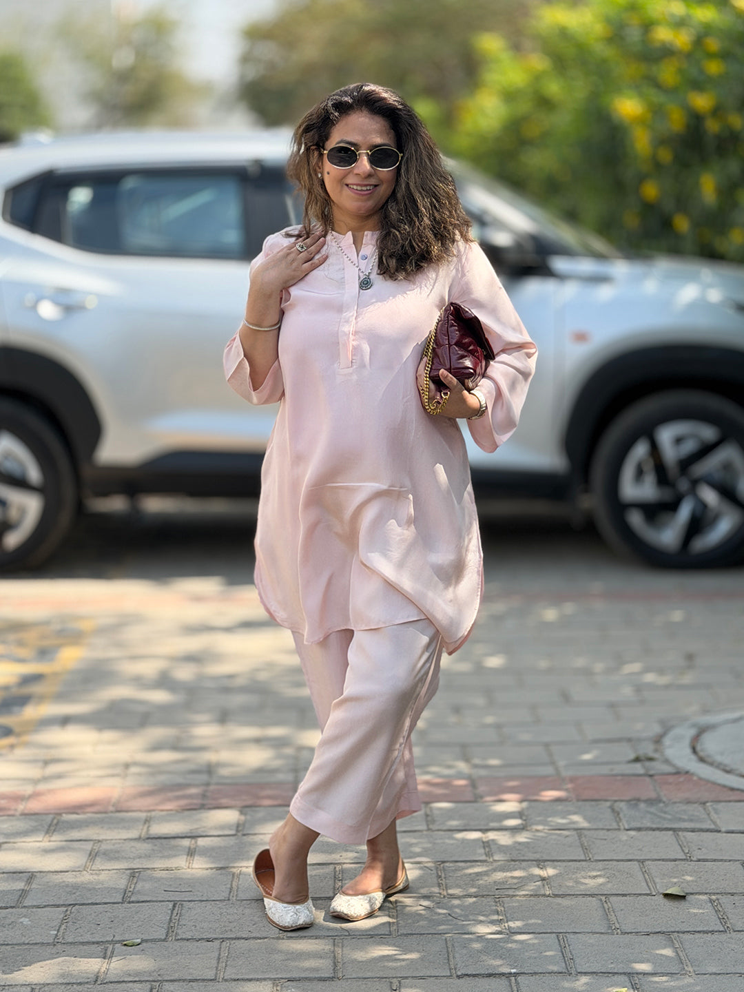 Woman in a light pink outfit standing on a street with a car in the background