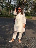 Woman in a white outfit standing on a paved area with trees in the background