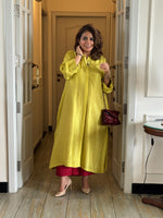 Woman in a yellow dress standing in a room with wooden flooring and a lamp.