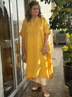 Woman in a yellow kurta standing outdoors near a building entrance.