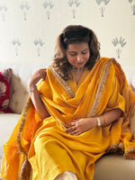 Woman in a yellow saree sitting on a couch with a neutral background
