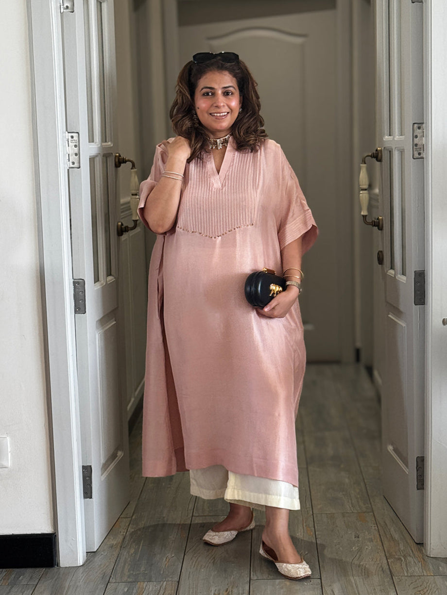 Woman in a pink dress standing in a hallway holding a Sabyasachi clutch.