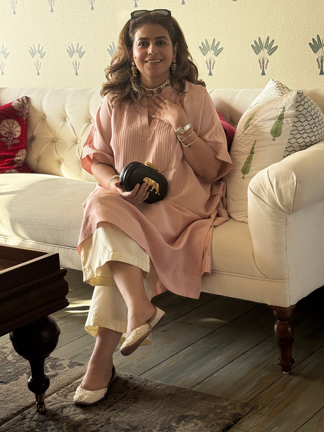 Woman sitting on a couch holding a black clutch in a living room.