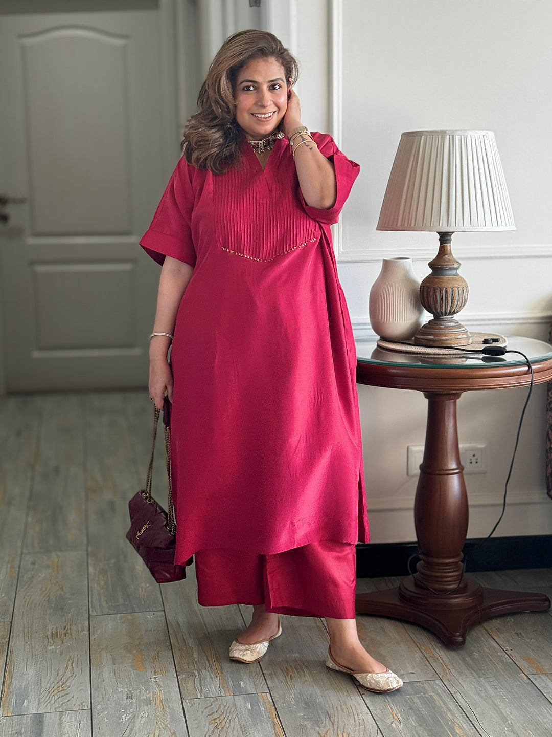 Woman in a pink dress standing in a room with a wooden table and lamp.