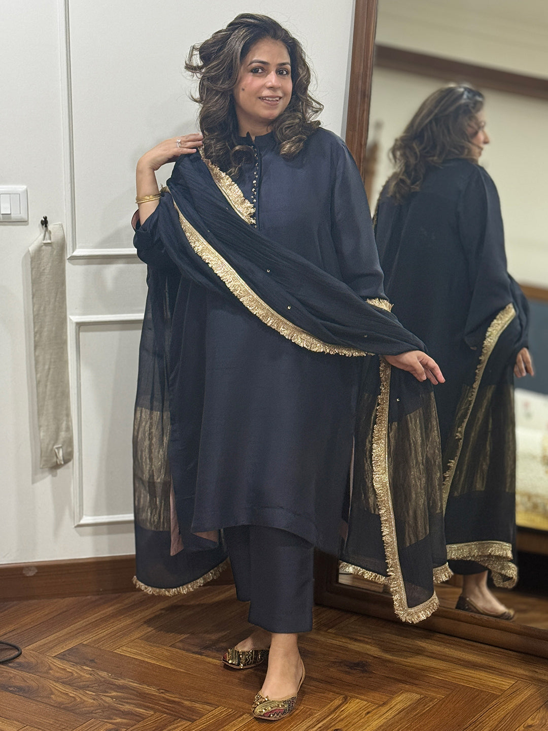 Woman wearing a dark black traditional silk kurta with gold trim on placket. Paired with Dupatta.