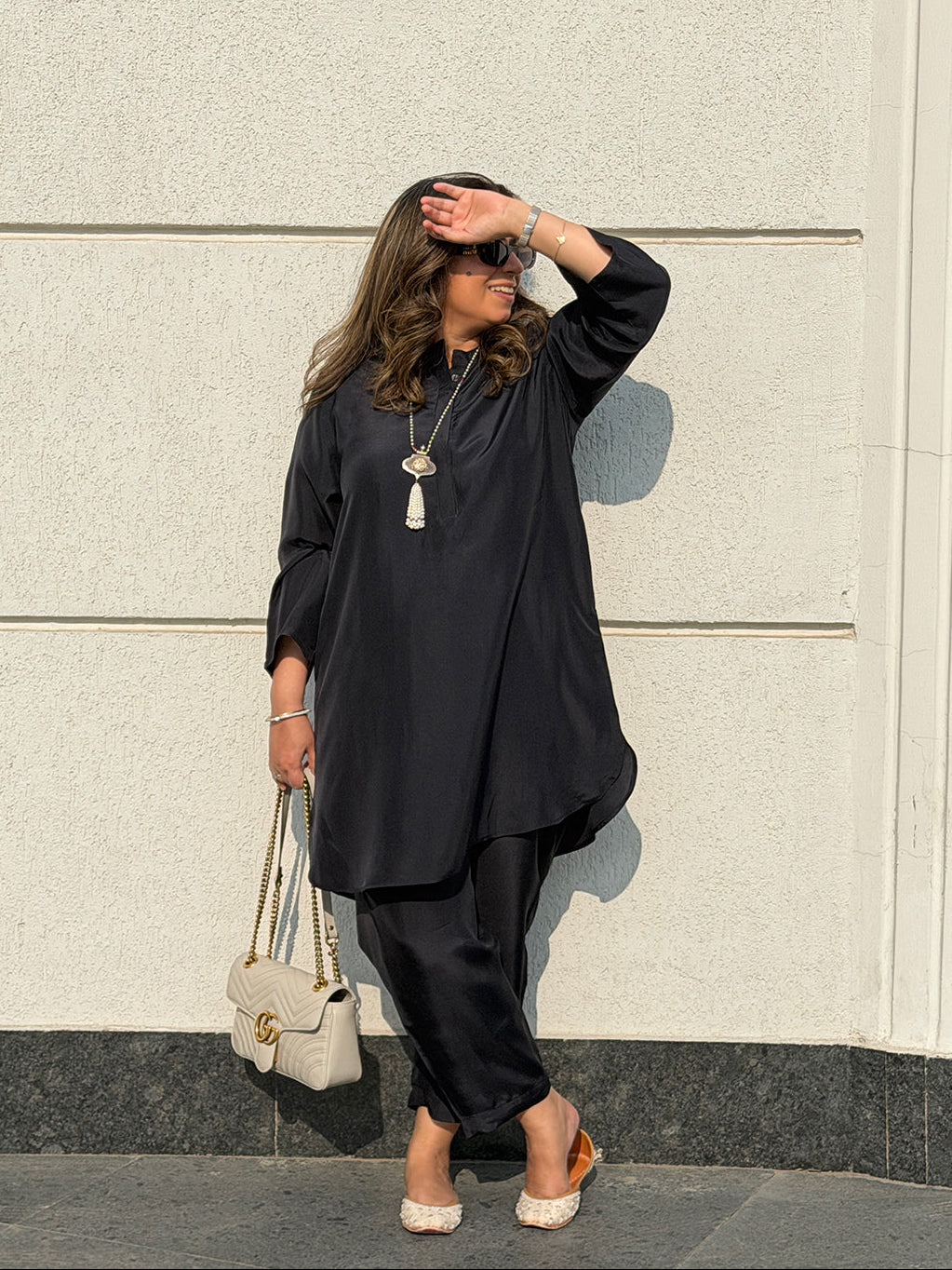 Woman in a black outfit standing against a light-colored wall.