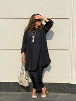 Woman in a black outfit standing against a light-colored wall.