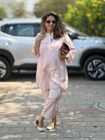 Woman in a light pink outfit standing on a street with a car in the background