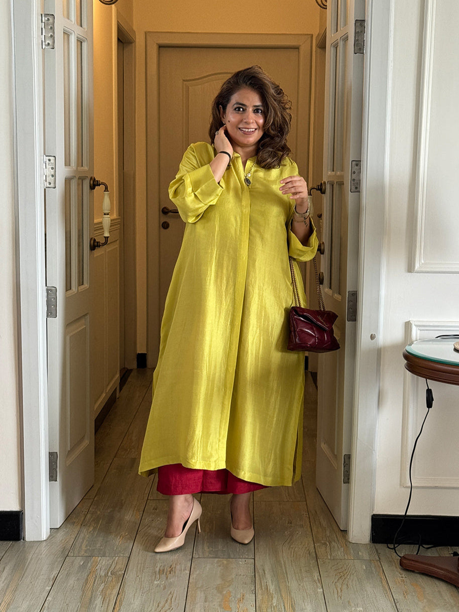 Woman in a yellow dress standing in a room with wooden flooring and a lamp.