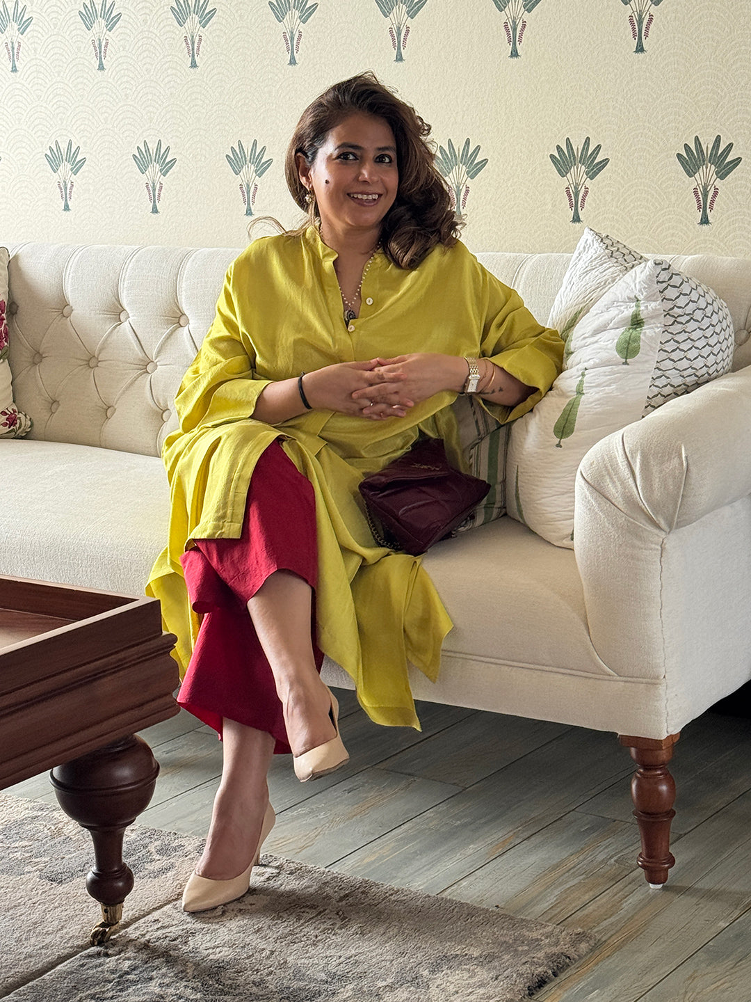 Woman in yellow kurta sitting on a white sofa with decorative pillows.