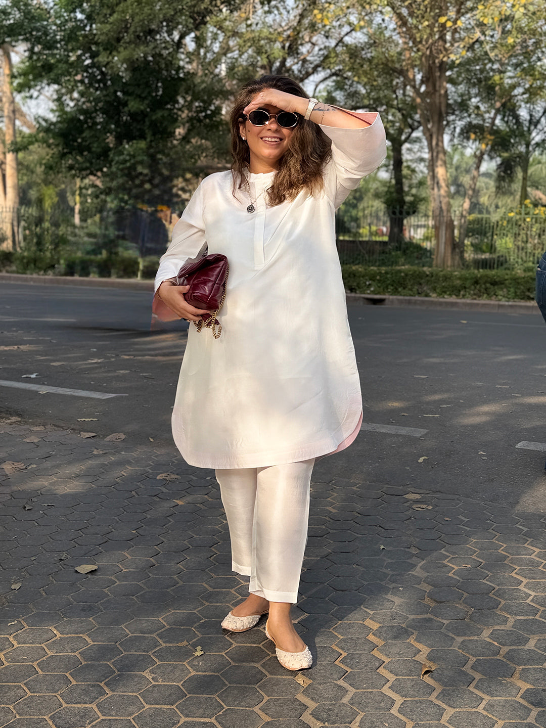 Woman in a white outfit standing on a paved area with trees in the background