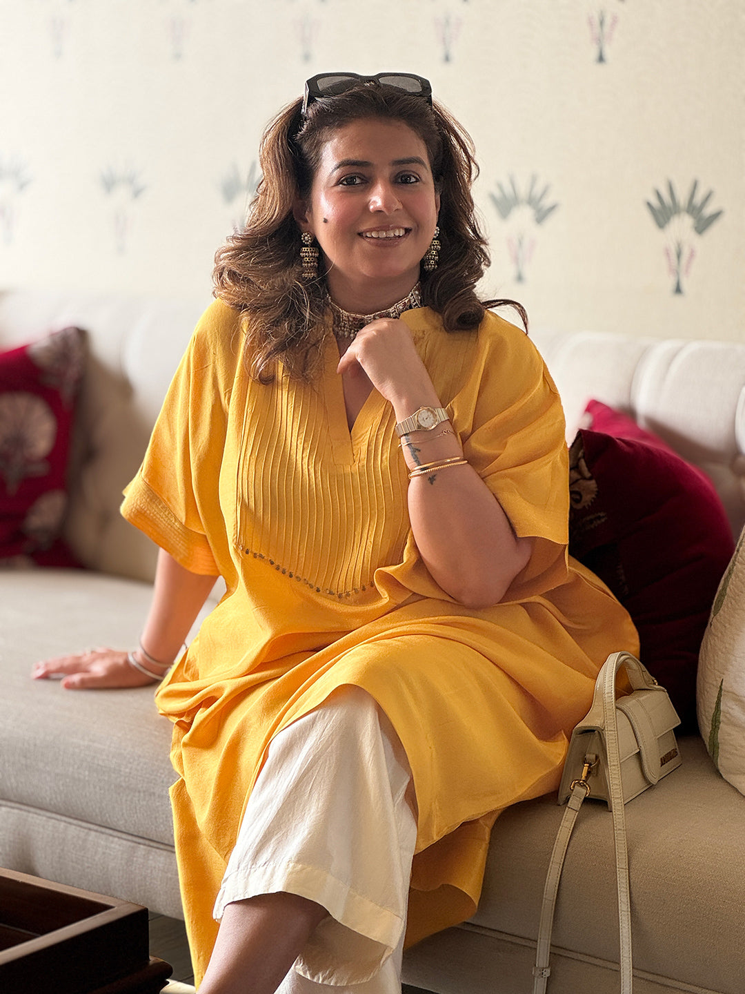 Woman in a yellow dress sitting on a couch with a decorative wall in the background