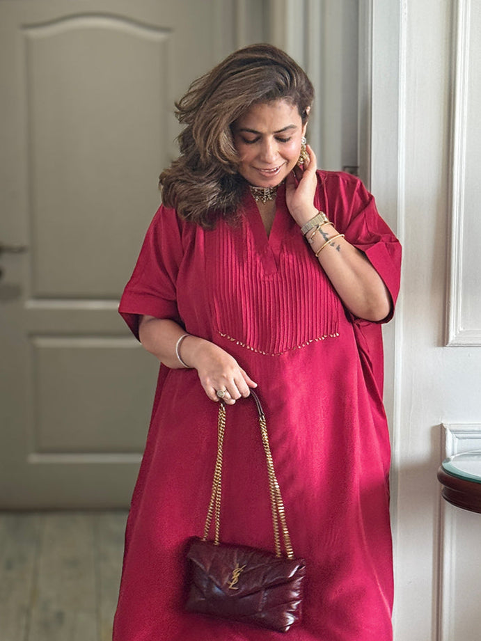Woman in a red dress holding a matching handbag in a room with a wooden table and lamp.