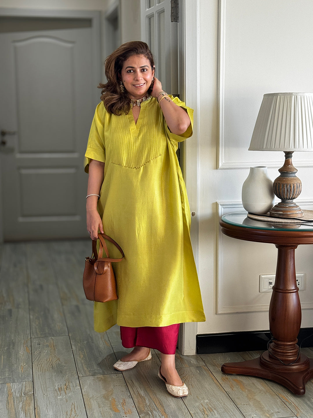 Woman in a yellow dress holding a brown handbag indoors.