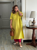 Woman in a yellow dress holding a brown handbag indoors.