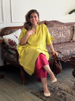 Woman in a yellow top and pink skirt sitting on a patterned sofa.