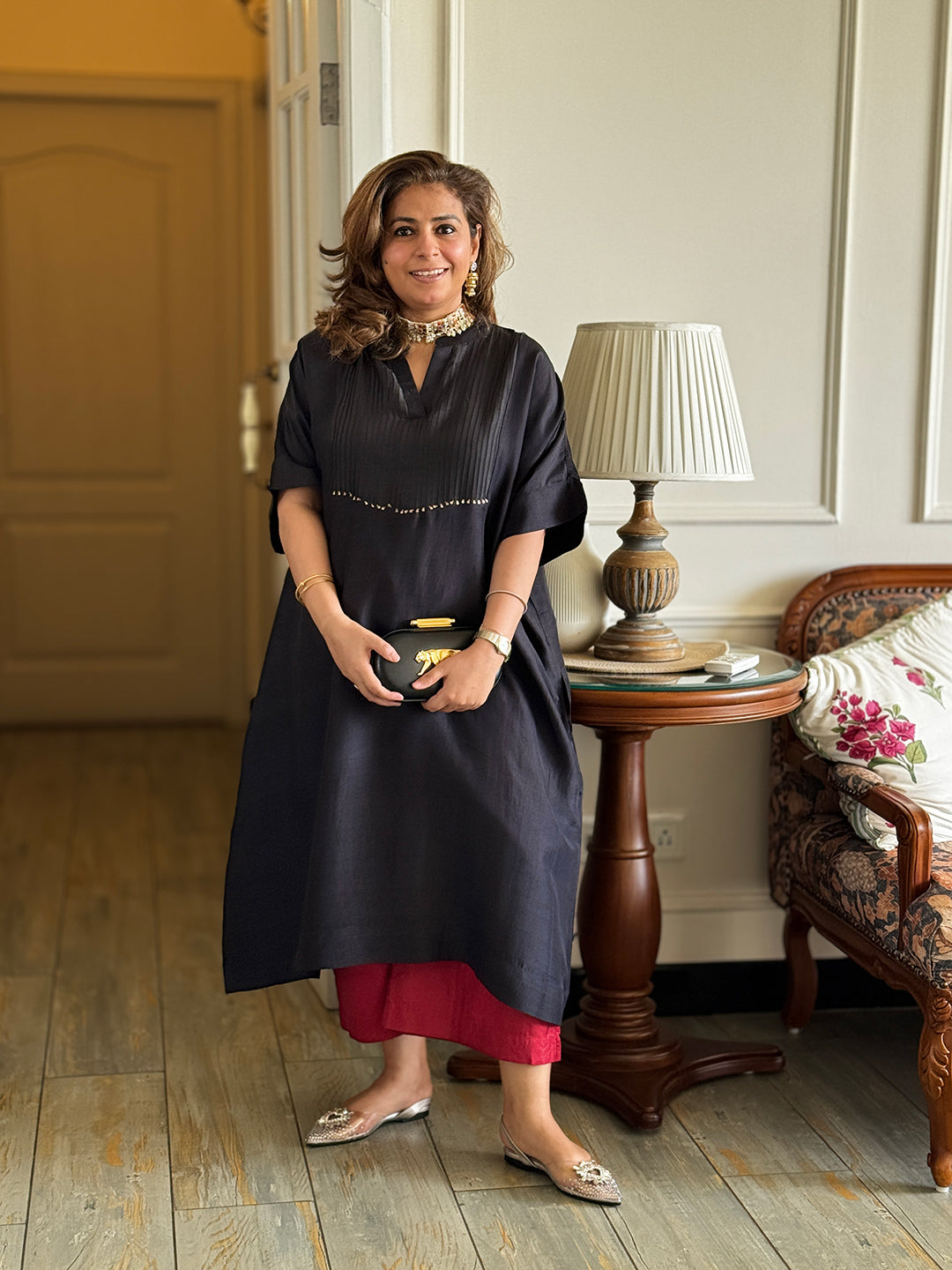 Woman in a black dress standing in a room with wooden flooring and a lamp in the background.