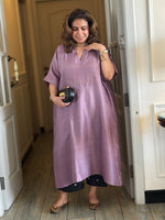 Woman in a purple dress standing in a room with wooden flooring.
