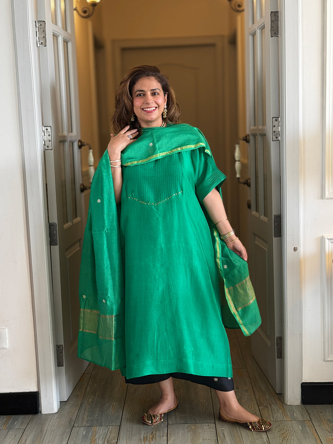 Woman wearing a green traditional outfit standing in a doorway.
