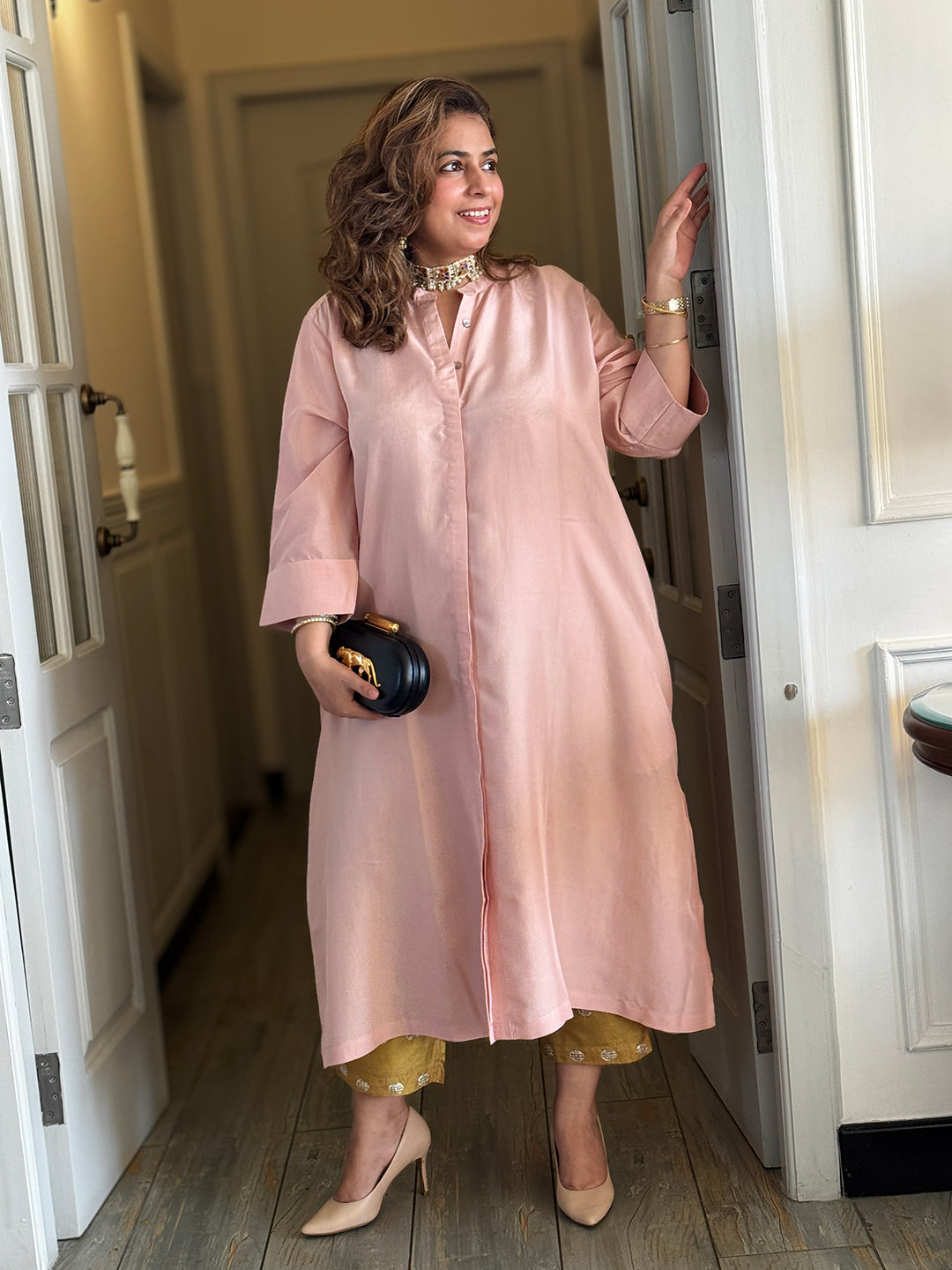 Woman in a long pink satin dress standing in a doorway.