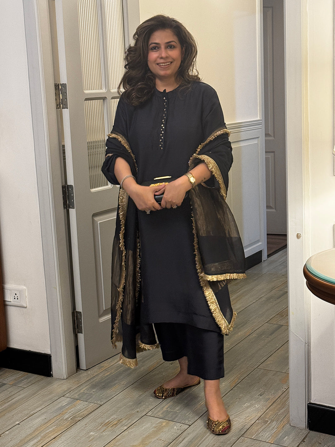 Woman wearing a dark black traditional silk kurta with gold trim on placket. Paired with embroidered Dupatta.