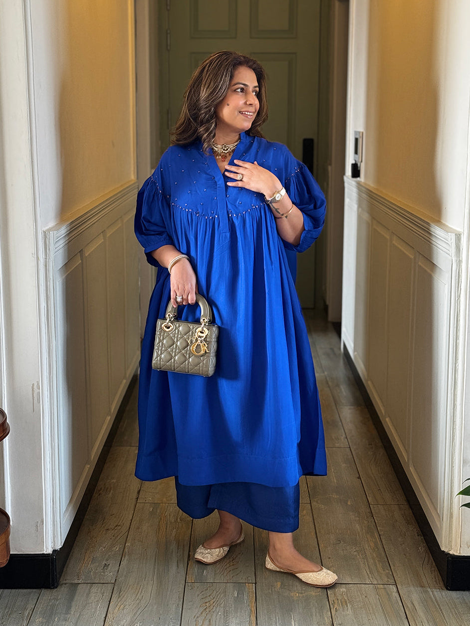 Woman in a blue dress holding a small handbag in a hallway.